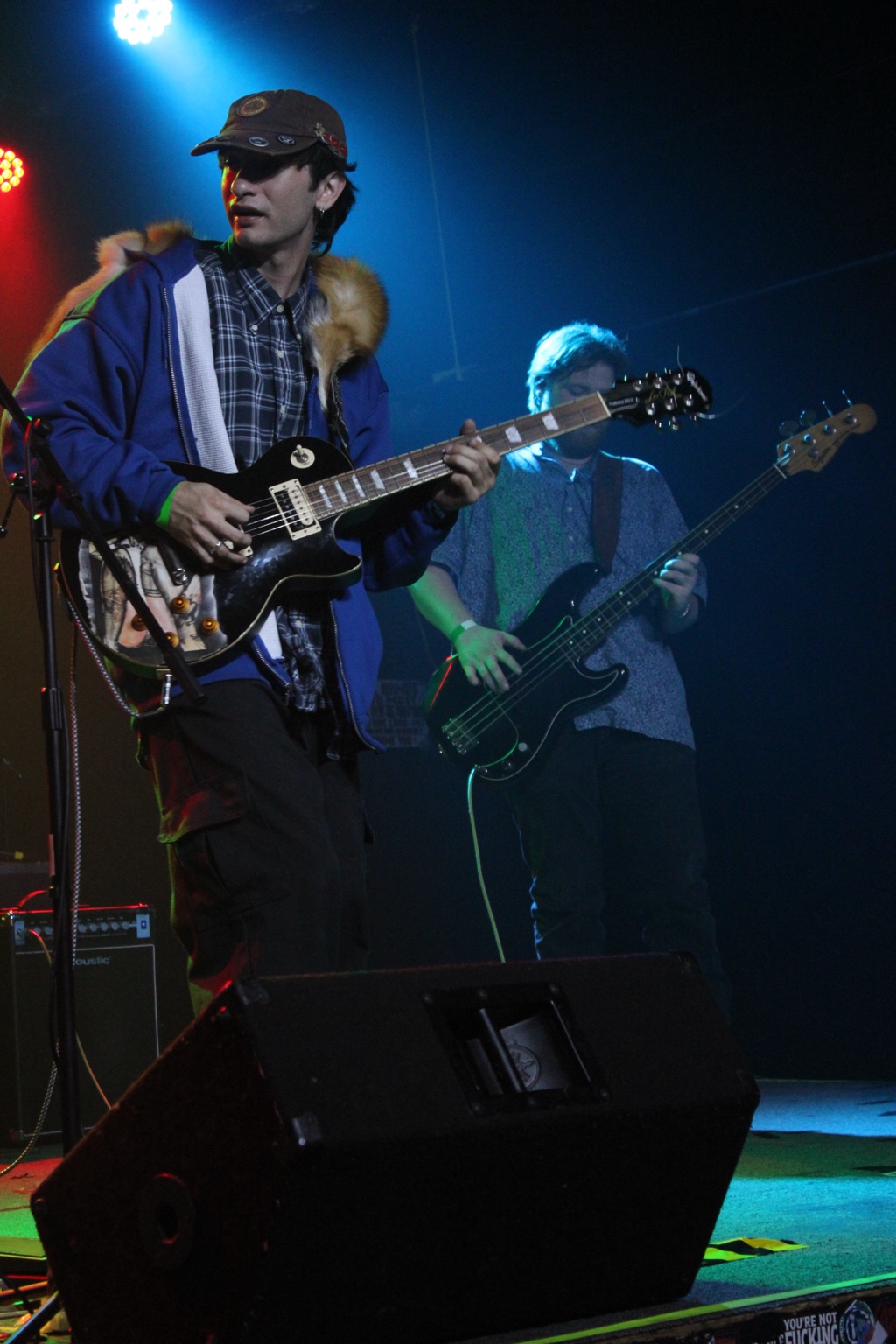 A guitarist and bassist performing beneath blue stage lighting.